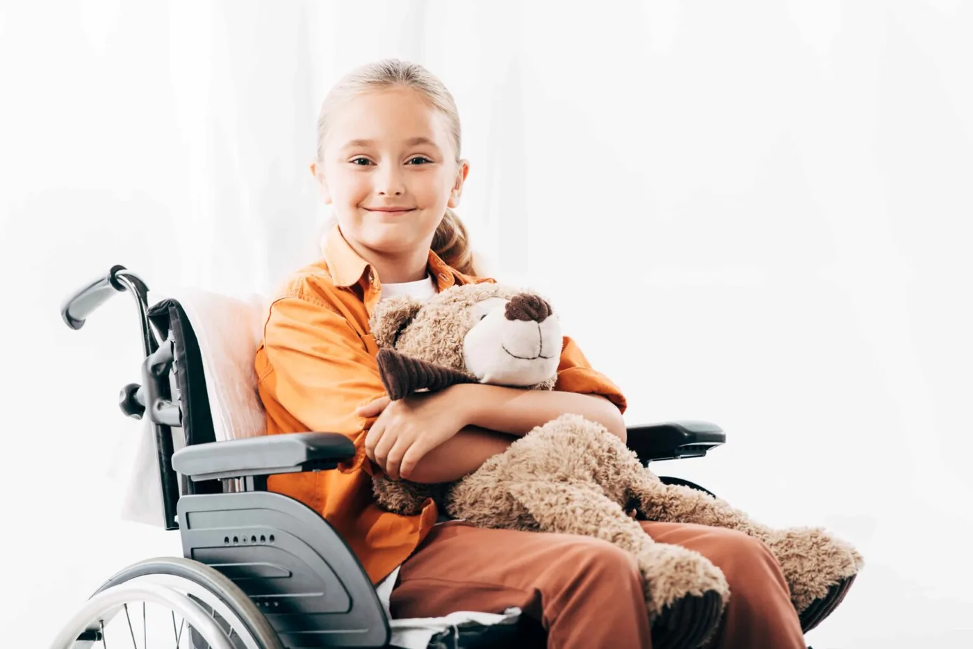 Smiling child holding a teddy bear in a wheelchair